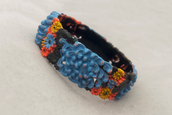 Horizontal perspective view of 1930s vintage blue, black, and yellow painted and floral carved coral mum celluloid bangle bracelet.