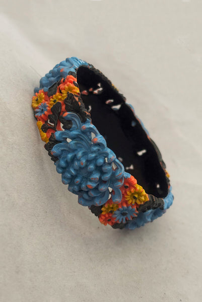 Vertical perspective view of 1930s vintage blue, black, and yellow painted and floral carved coral mum celluloid bangle bracelet.
