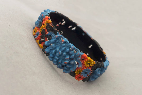 Horizontal perspective view of 1930s vintage blue, black, and yellow painted and floral carved coral mum celluloid bangle bracelet.