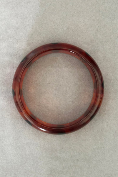 Vertical top view of contemporary artisan Christopher Dombek root beer translucent brown Bakelite domed bangle bracelet with inlaid oval black dots.