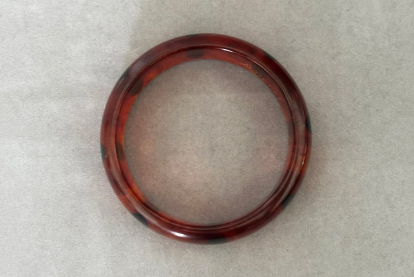 Horizontal top view of contemporary artisan Christopher Dombek root beer translucent brown Bakelite domed bangle bracelet with inlaid oval black dots.