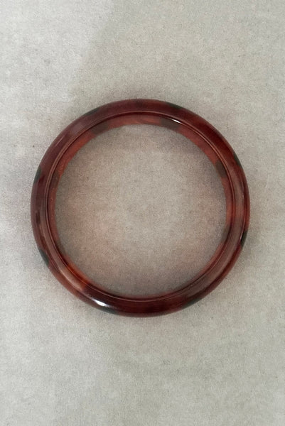 Vertical bottom view of contemporary artisan Christopher Dombek root beer translucent brown Bakelite domed bangle bracelet with inlaid oval black dots.