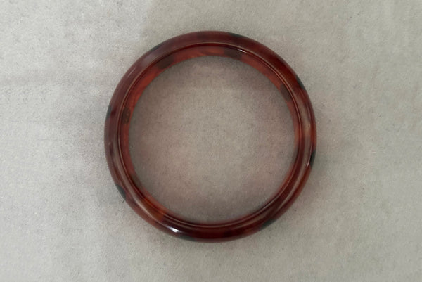 Horizontal bottom view of contemporary artisan Christopher Dombek root beer translucent brown Bakelite domed bangle bracelet with inlaid oval black dots.