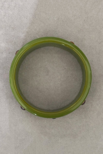 Vertical top view of 1960s vintage striated green plastic bangle bracelet with gold tone studs.