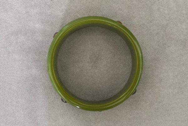 Horizontal top view of 1960s vintage striated green plastic bangle bracelet with gold tone studs.