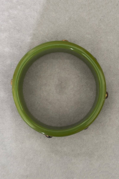 Vertical bottom view of 1960s vintage striated green plastic bangle bracelet with gold tone studs.
