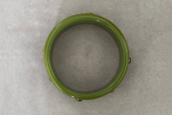 Horizontal bottom view of 1960s vintage striated green plastic bangle bracelet with gold tone studs.