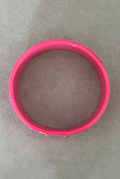 Vertical top view of 1980s vintage pink plastic oval bangle bracelet with gold tone metal studs. Showing a seam on the bangle.