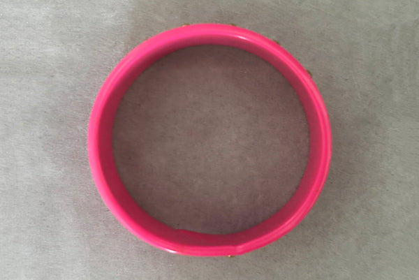 Horizontal top view of 1980s vintage pink plastic oval bangle bracelet with gold tone metal studs. Showing a seam on the bangle.