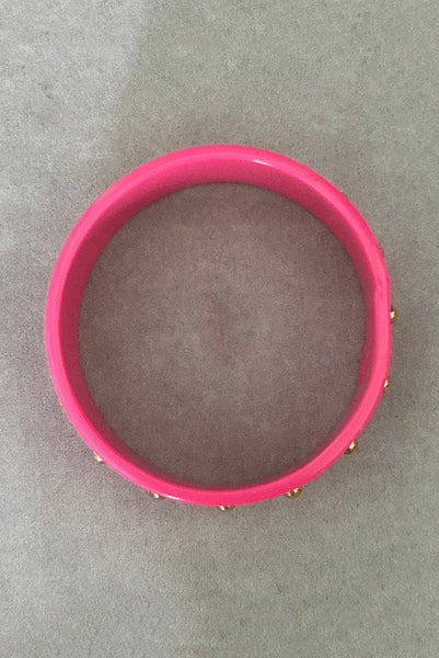 Vertical bottom view of 1980s vintage pink plastic oval bangle bracelet with gold tone metal studs. Showing a seam on the bangle.