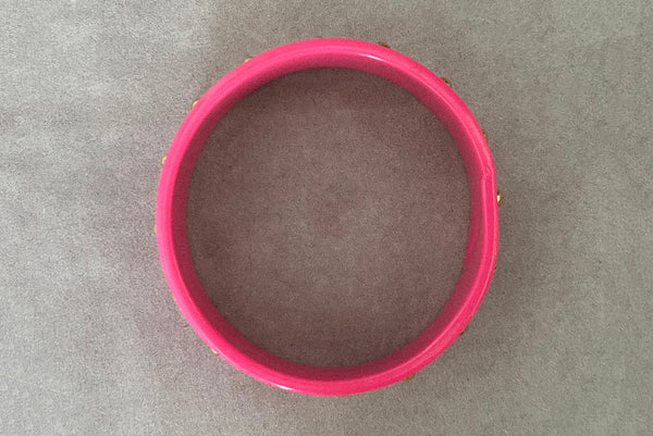 Horizontal bottom view of 1980s vintage pink plastic oval bangle bracelet with gold tone metal studs. Showing a seam on the bangle.