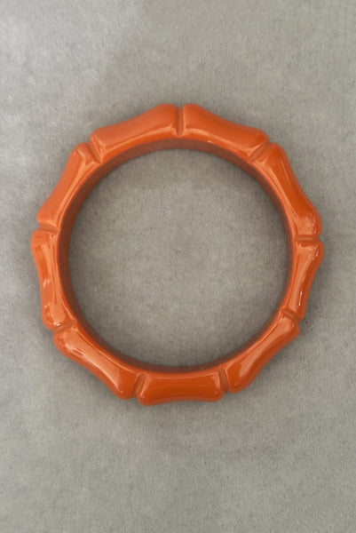 Vertical bottom view of 2000s y2k vintage orange plastic molded faux bamboo bangle bracelet.