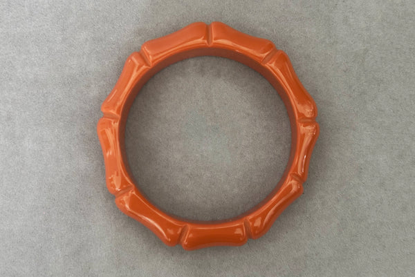 Horizontal bottom view of 2000s y2k vintage orange plastic molded faux bamboo bangle bracelet.