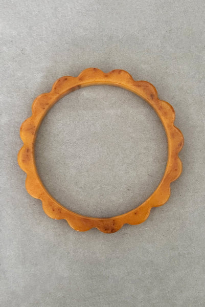 Vertical top view of 1930s vintage pair of yellow marbled egg yolk and butterscotch scalloped or daisy Bakelite bangle bracelet set of two (2). Showing the butterscotch bangle alone.