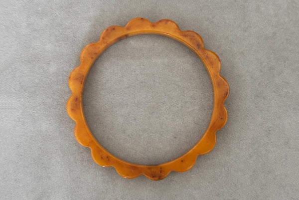 Horizontal top view of 1930s vintage pair of yellow marbled egg yolk and butterscotch scalloped or daisy Bakelite bangle bracelet set of two (2). Showing the butterscotch bangle alone.