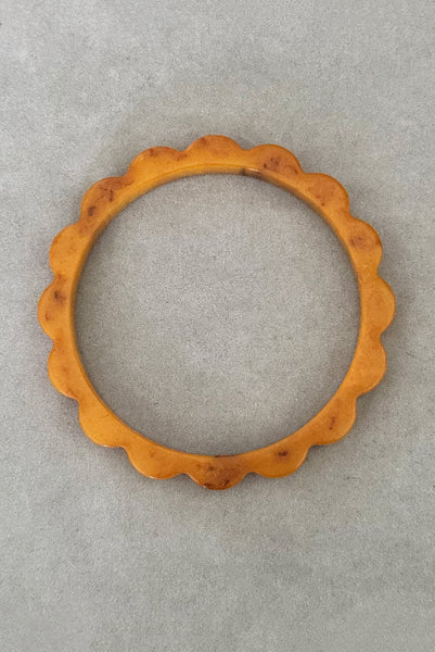 Vertical bottom view of 1930s vintage pair of yellow marbled egg yolk and butterscotch scalloped or daisy Bakelite bangle bracelet set of two (2). Showing the butterscotch bangle alone.
