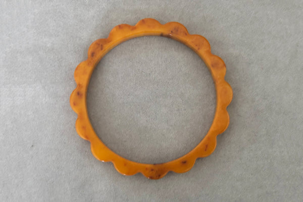 Horizontal bottom view of 1930s vintage pair of yellow marbled egg yolk and butterscotch scalloped or daisy Bakelite bangle bracelet set of two (2). Showing the butterscotch bangle alone.