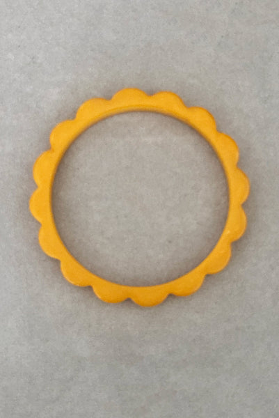 Vertical top view of 1930s vintage pair of yellow marbled egg yolk and butterscotch scalloped or daisy Bakelite bangle bracelet set of two (2). Showing the egg yolk bangle alone.