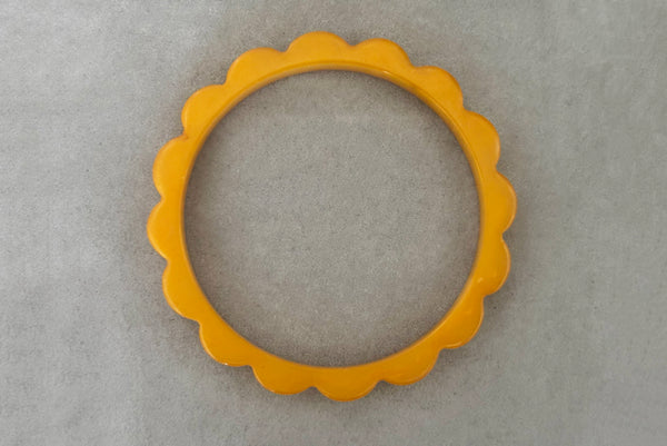 Horizontal top view of 1930s vintage pair of yellow marbled egg yolk and butterscotch scalloped or daisy Bakelite bangle bracelet set of two (2). Showing the egg yolk bangle alone.