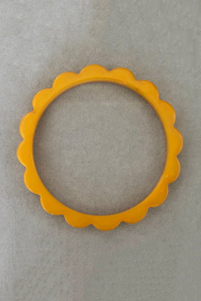 Vertical bottom view of 1930s vintage pair of yellow marbled egg yolk and butterscotch scalloped or daisy Bakelite bangle bracelet set of two (2). Showing the egg yolk bangle alone.