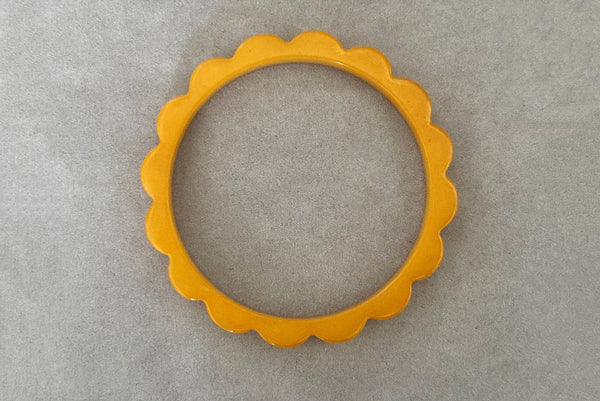 Horizontal bottom view of 1930s vintage pair of yellow marbled egg yolk and butterscotch scalloped or daisy Bakelite bangle bracelet set of two (2). Showing the egg yolk bangle alone.
