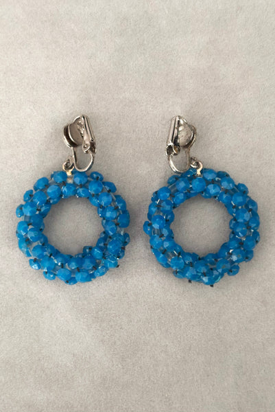 Vertical back view of 1950s vintage rhinestone, silver tone, and blue plastic beaded hoop clip-on statement earrings.