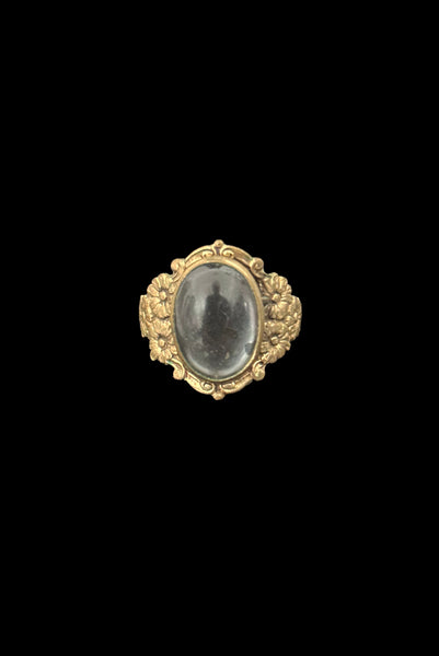 Vertical front view of 1990s vintage Victorian style floral brass ring with bezel set oval gray glass cabochon, size 8.