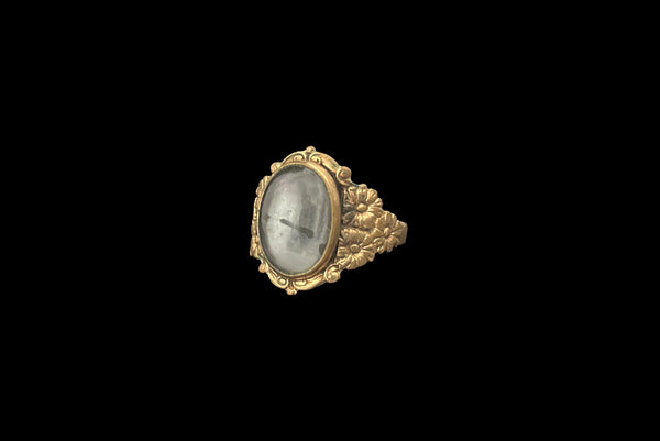 Horizontal perspective view of 1990s vintage Victorian style floral brass ring with bezel set oval gray glass cabochon, size 8.