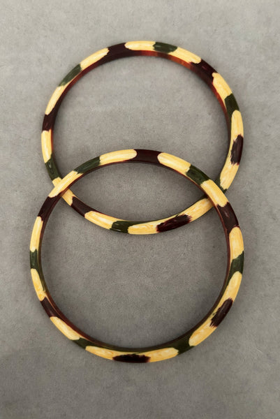 Vertical top view of 1960s vintage cream, purple, and green celluloid two (2) bangle bracelet set. Showing the pair of bangles together.
