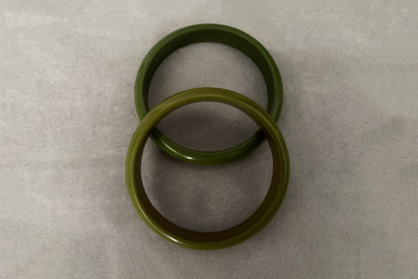 Horizontal top view of 1980s vintage green plastic two (2) bangle bracelet set inlaid with gold tone brass dots. Showing the two bangles together.