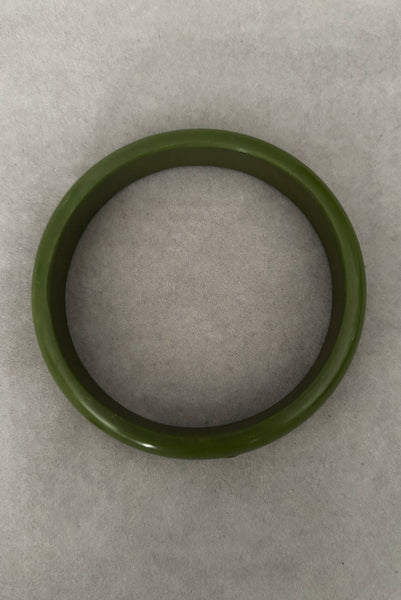 Vertical top view of 1980s vintage green plastic two (2) bangle bracelet set inlaid with gold tone brass dots. Showing the darker bangle.