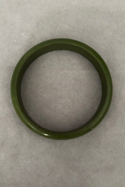 Vertical bottom view of 1980s vintage green plastic two (2) bangle bracelet set inlaid with gold tone brass dots. Showing the darker bangle.