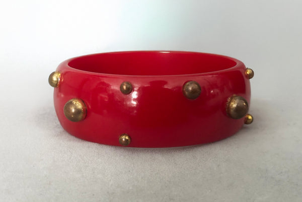 Horizontal front view of 1940s vintage brass studded rich cherry red Bakelite statement bangle bracelet.
