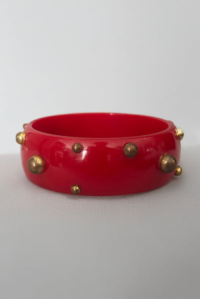 Vertical front view of 1940s vintage brass studded rich cherry red Bakelite statement bangle bracelet.