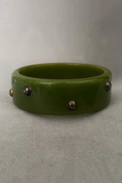 Vertical front view of 1960s vintage striated green plastic bangle bracelet with gold tone studs. Showing discoloration of the studs.