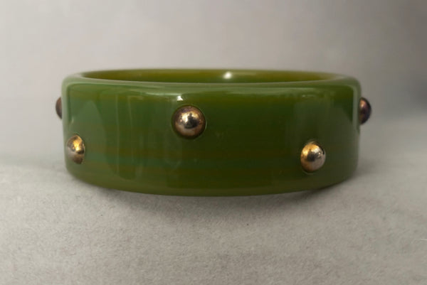 Horizontal back view of 1960s vintage striated green plastic bangle bracelet with gold tone studs. Showing discoloration of the studs.