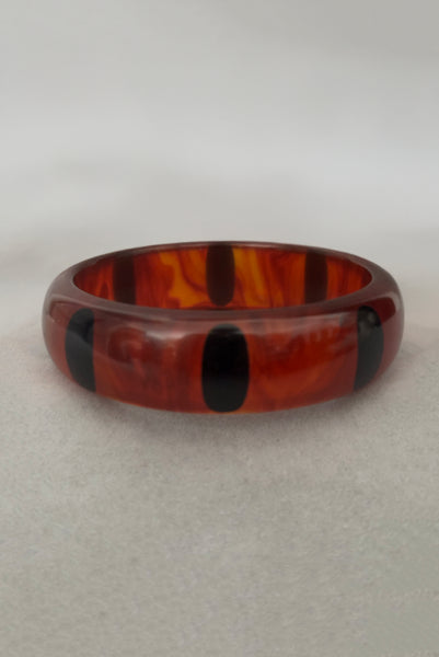Vertical front view of contemporary artisan Christopher Dombek root beer translucent brown Bakelite domed bangle bracelet with inlaid oval black dots.