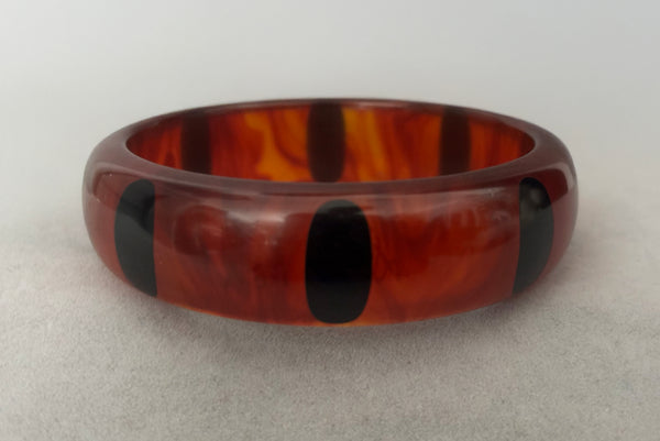 Horizontal front view of contemporary artisan Christopher Dombek root beer translucent brown Bakelite domed bangle bracelet with inlaid oval black dots.