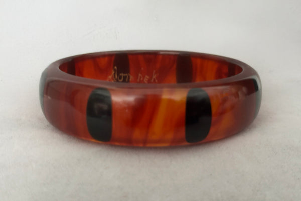 Horizontal back view of contemporary artisan Christopher Dombek root beer translucent brown Bakelite domed bangle bracelet with inlaid oval black dots.