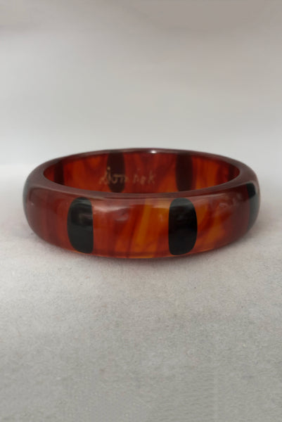 Vertical back view of contemporary artisan Christopher Dombek root beer translucent brown Bakelite domed bangle bracelet with inlaid oval black dots.