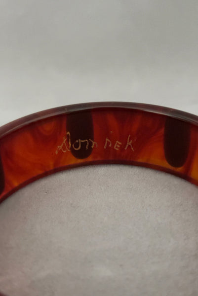 Detail view of contemporary artisan Christopher Dombek root beer translucent brown Bakelite domed bangle bracelet with inlaid oval black dots. Showing the engraved Dombek signature.