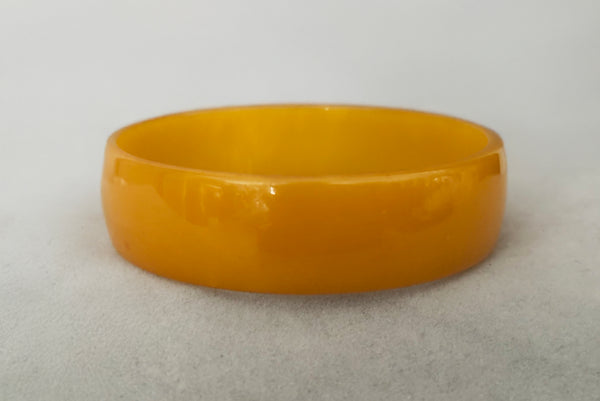 Horizontal front view of 1940s vintage egg yolk yellow and mustard marbled Bakelite domed bangle bracelet