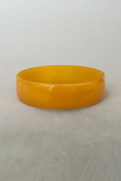 Vertical front view of 1940s vintage egg yolk yellow and mustard marbled Bakelite domed bangle bracelet