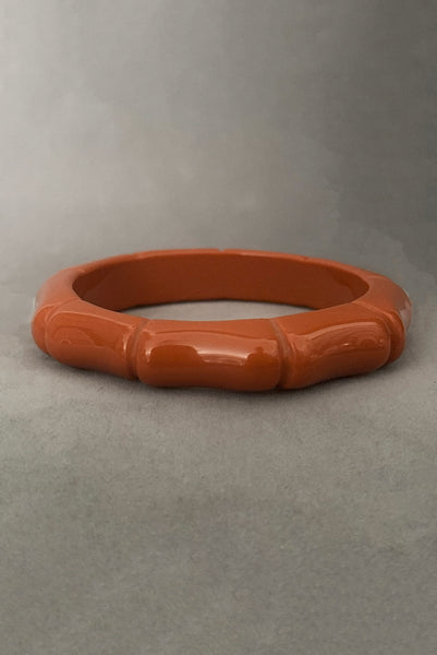 Vertical front view of 2000s y2k vintage orange plastic molded faux bamboo bangle bracelet.