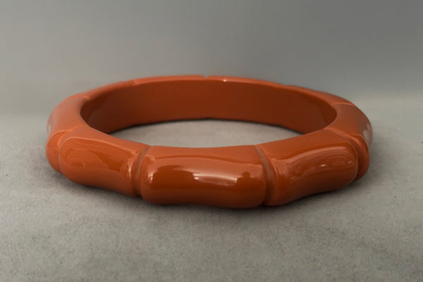 Horizontal front view of 2000s y2k vintage orange plastic molded faux bamboo bangle bracelet.