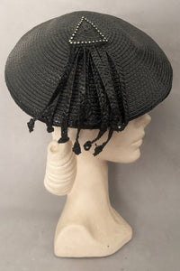 Vertical side view of 1960s vintage rhinestone trimmed black glossy straw beret with straw fringe, by Jack McConnell.