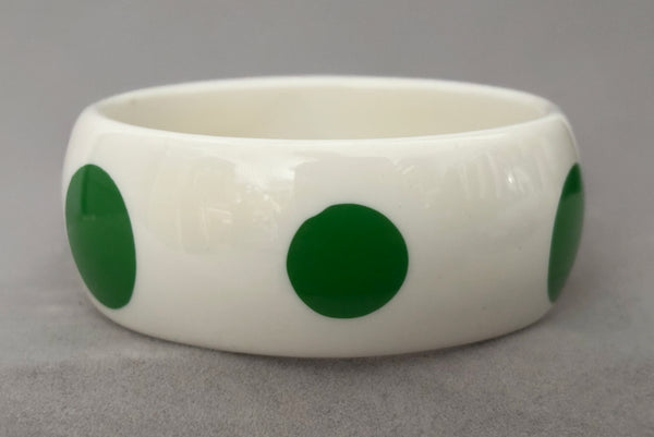 Horizontal side view of 1980s vintage green and white polka dot plastic domed bangle bracelet.