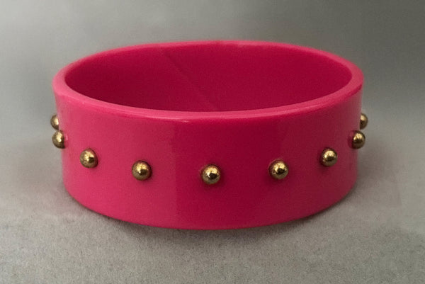 Horizontal front view of 1980s vintage pink plastic oval bangle bracelet with gold tone metal studs.