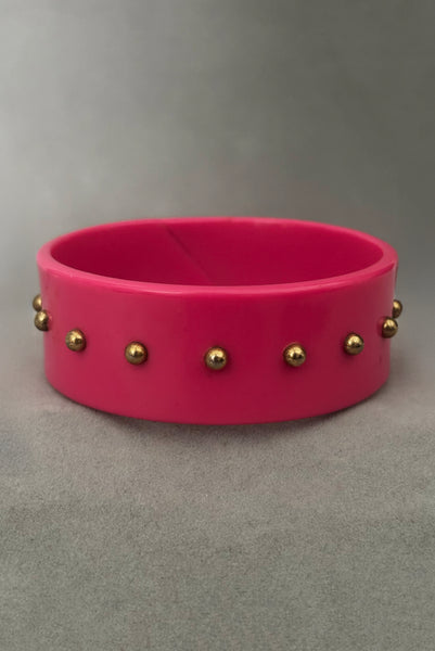 Vertical front view of 1980s vintage pink plastic oval bangle bracelet with gold tone metal studs.