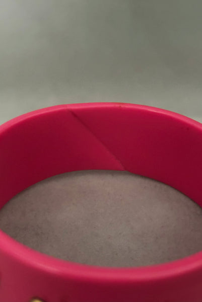 Detail view of 1980s vintage pink plastic oval bangle bracelet with gold tone metal studs. Showing a seam on the bangle.